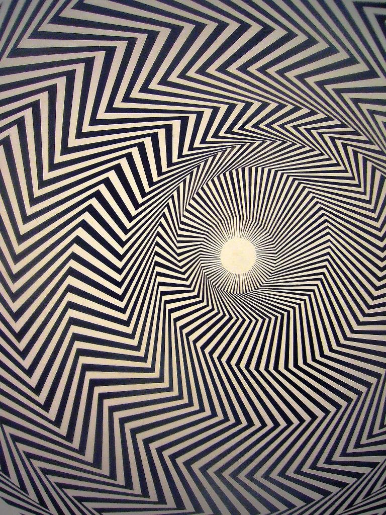 Optical illusion with black and white zigzag lines creating a swirling spiral pattern centered around a bright white point.